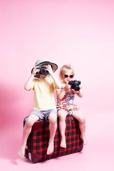 Viajes: Niños un niño y una niña juegan en los turistas, se sientan en una gran maleta roja y toman fotos. —  Fotos de Stock