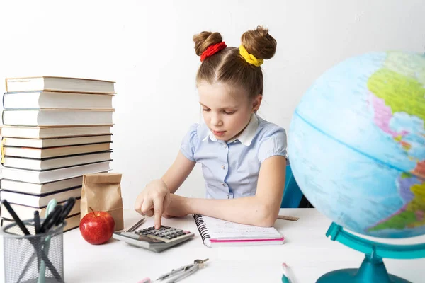 Повернутися до школи: дівчина сидить за столом і робить розрахунки на калькуляторі . — стокове фото