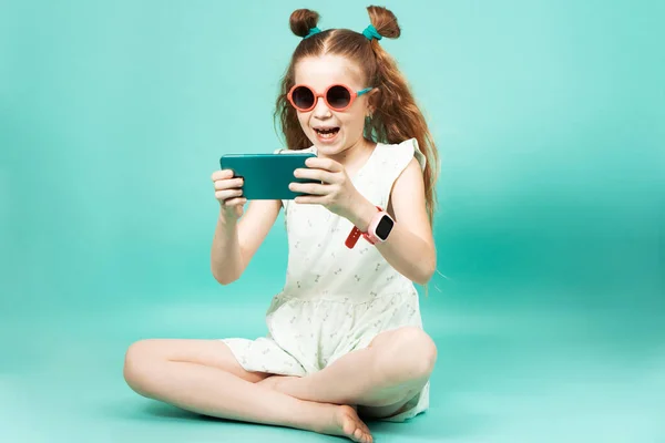 Mobile gaming: a girl in sunglasses sits and plays on a smartphone.