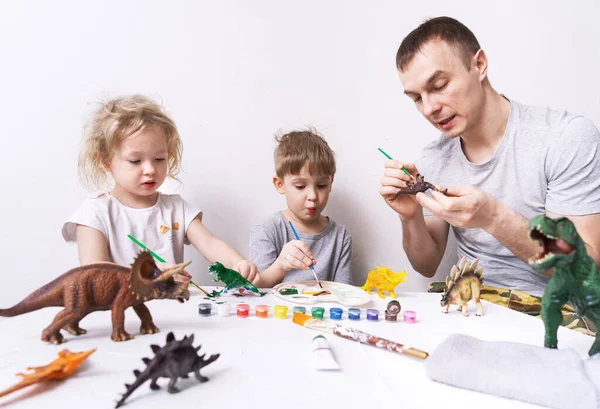 Hobby: pai com filho e filha pintar pequenas figuras de dinossauros com tinta e uma escova. — Fotografia de Stock
