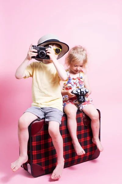 Viajes: Niños un niño y una niña juegan en los turistas, se sientan en una gran maleta roja y toman fotos. —  Fotos de Stock