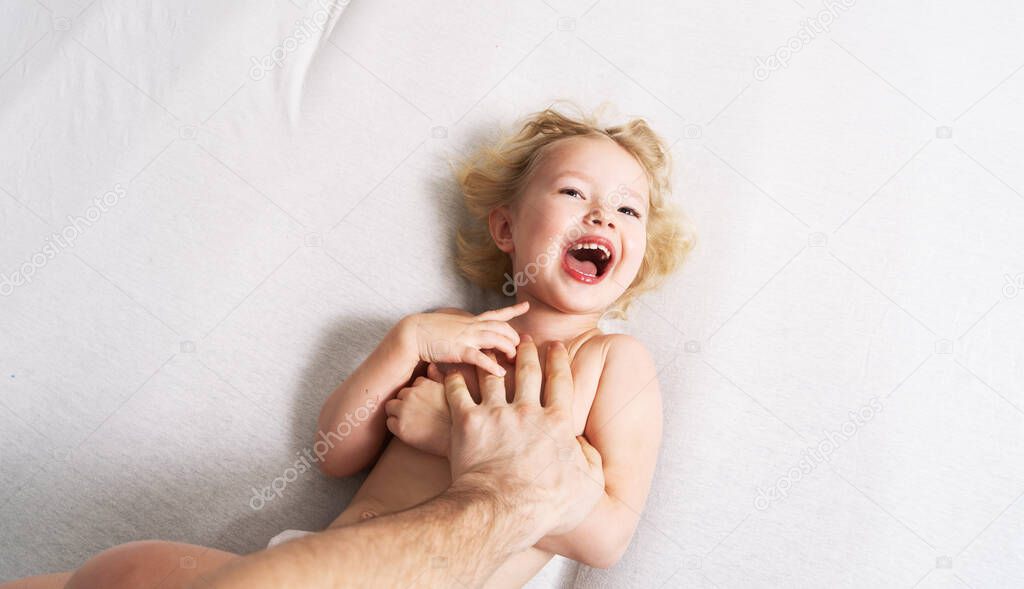 Family time: a little girl lies on the bed and laughs cheerfully because of the tickling of her father.
