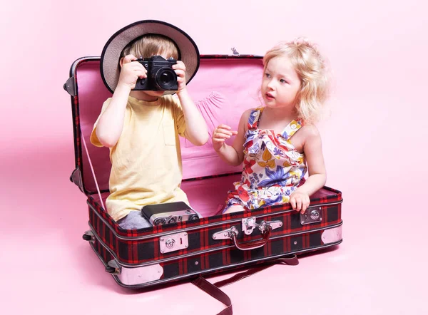 Viajes: Niños un niño y una niña juegan en los turistas, se sientan en una gran maleta roja y toman fotos en la cámara. — Foto de Stock