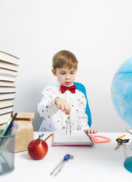 Назад до школи: Хлопчик сидить за столом і малює в блокноті за допомогою циркуля . — стокове фото