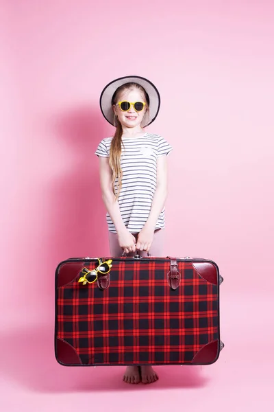 Podróż: Mała dziewczynka w słomkowym kapeluszu trzyma dużą czerwoną walizkę i czeka na wycieczkę. — Zdjęcie stockowe