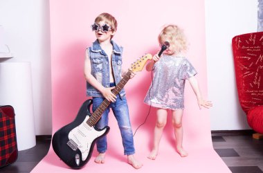 Pop Culture: Çocuklar gitarlı bir oğlan ve mikrofonlu bir kız popüler müzisyenler gibi davranıp bir ev konseri veriyorlar. Pembe arka planda bir portre.