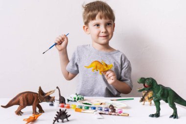 Hobi: bir çocuk, bir anaokulu öğrencisi, fırça ve püskülle resim yapıyor bir dinozor oyuncağının küçük bir figürü.