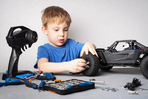 Modelos controlados por rádio: Um menino em uma camiseta azul está reparando seu buggy RC. — Fotografia de Stock