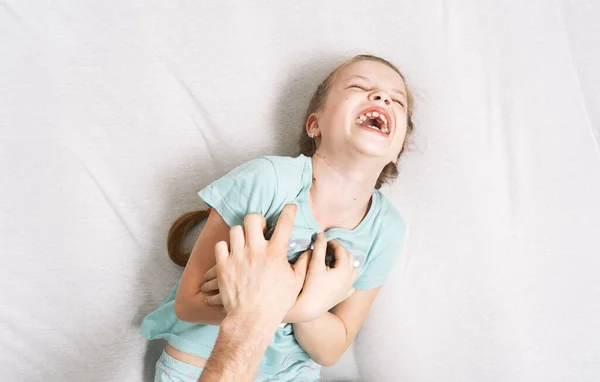 家族の時間:小さな女の子がベッドの上に横たわって、彼女の父のくすぐるさのために陽気に笑う. — ストック写真