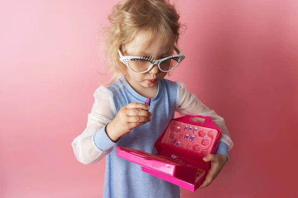 Niña pequeña juega con un conjunto de cosméticos para bebés y usa lápiz labial. — Foto de Stock
