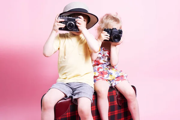 Ταξίδια: Τα παιδιά ένα μικρό αγόρι και ένα κορίτσι παίζουν στους τουρίστες, κάθονται σε μια μεγάλη κόκκινη βαλίτσα και να τραβήξετε φωτογραφίες. — Φωτογραφία Αρχείου