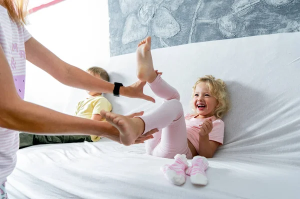 Anne küçük kızının ayaklarını gıdıklıyor. Kız neşeyle gülüyor..