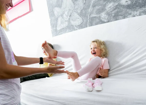 Mamá hace cosquillas en los pies de sus hijas. La chica se ríe alegremente. —  Fotos de Stock