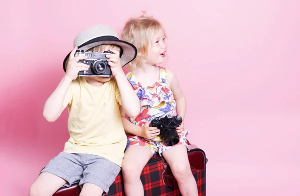 Viajes: Niños un niño y una niña juegan en los turistas, se sientan en una gran maleta roja y toman fotos. — Foto de Stock