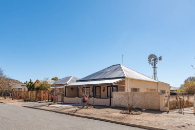 De Aar, Güney Afrika Cumhuriyeti, 6 Ağustos 2018: bir sokak sahne, eski evlerde De Aar, Northern Cape Eyaleti ile. Bir su pompalama yel değirmeni görülür