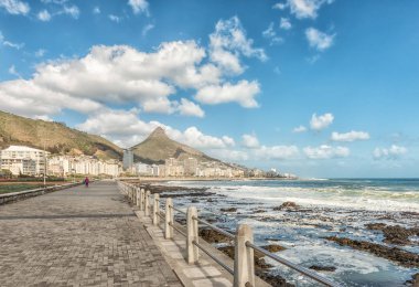 CAPE TOWN, SOUTH AFRICA, AUGUST 17, 2018: A walkway next to the sea at Mouille Point in Cape Town in the Western Cape Province. Apartment buildings, Signal Hill and Lions Head are visible in the back clipart