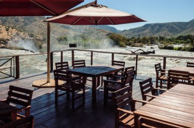 EPUPA, NAMIBIA - 25 Mayıs 2011: Kunene Nehri 'ndeki Epupa şelalesinin tepesindeki bir restoranın güvertesi. Masalar ve sandalyeler görünür.