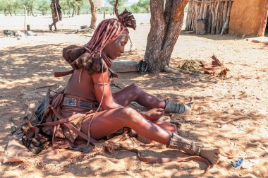 EPUPA, NAMIBIA - 27 Mayıs 2011: Geleneksel saç kilitleri ve süslü başlığı olan evli bir Himba kadını, öğütücü kırmızı mermer ile cildine sür ve bunu petrol jölesiyle karıştır