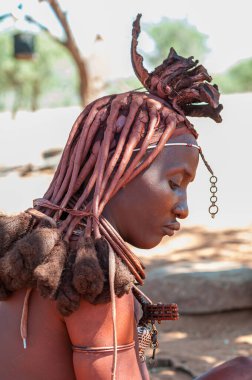 EPUPA, NAMIBIA - 27 Mayıs 2011: Epupa yakınlarındaki bir Himba köyünde fotoğrafçılara poz veren geleneksel saç kilitleri ve süslü başlıklı evli Himba kadınının profili