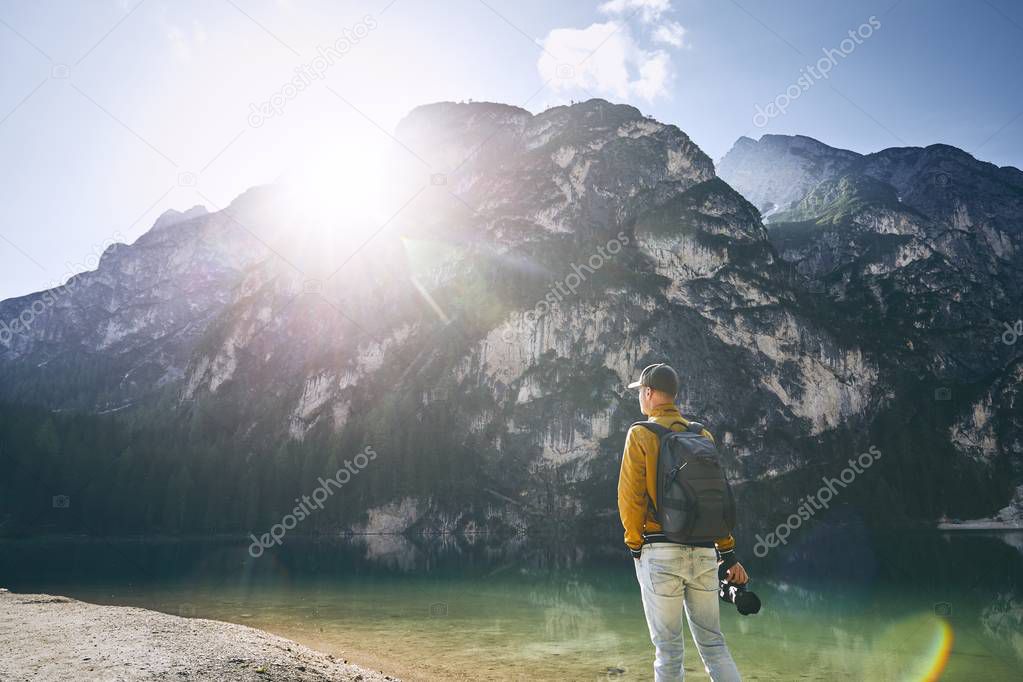 Young photographer holding camera against Lake Braies and mountains during sunrise. Dolomites, Italy 