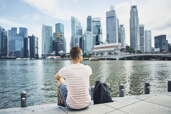 年轻人 旅行者 与背包坐在海滨反对新加坡的市中心和金融区 — 图库照片