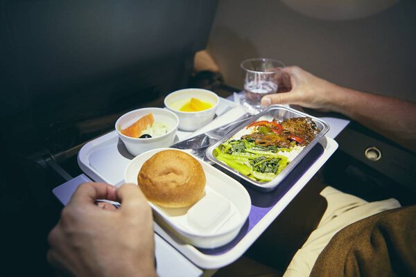 Traveling by airplane. Passenger enjoying dinner in economy class during long haul flight. 