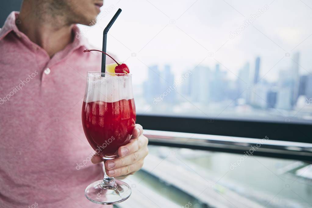 Young man drinking Singapore Sling drink against urban skyline of Singapore.