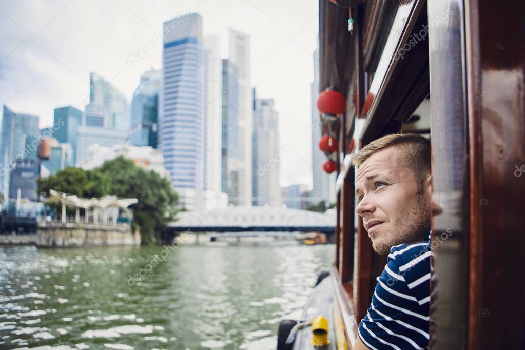 Young man exploring city and looking out from river boat in Singapore.