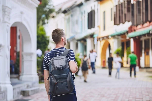 Traveler in city. Young man with backpack admiring architecture of old houses in Singapore.