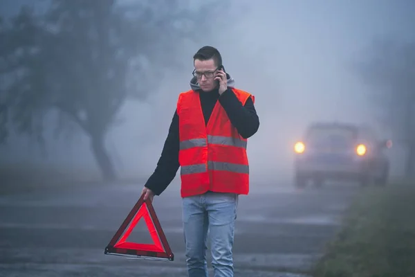 濃い霧にトラフィックの問題 若いドライバー サポートを求めて 彼の壊れた車の後ろに三角形の警告を入れて — ストック写真