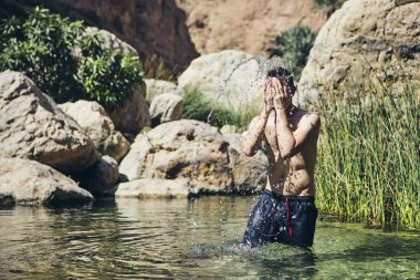 Young man splashing water on face. Refreshing in Wadi Shab, Sultanate of Oman. clipart