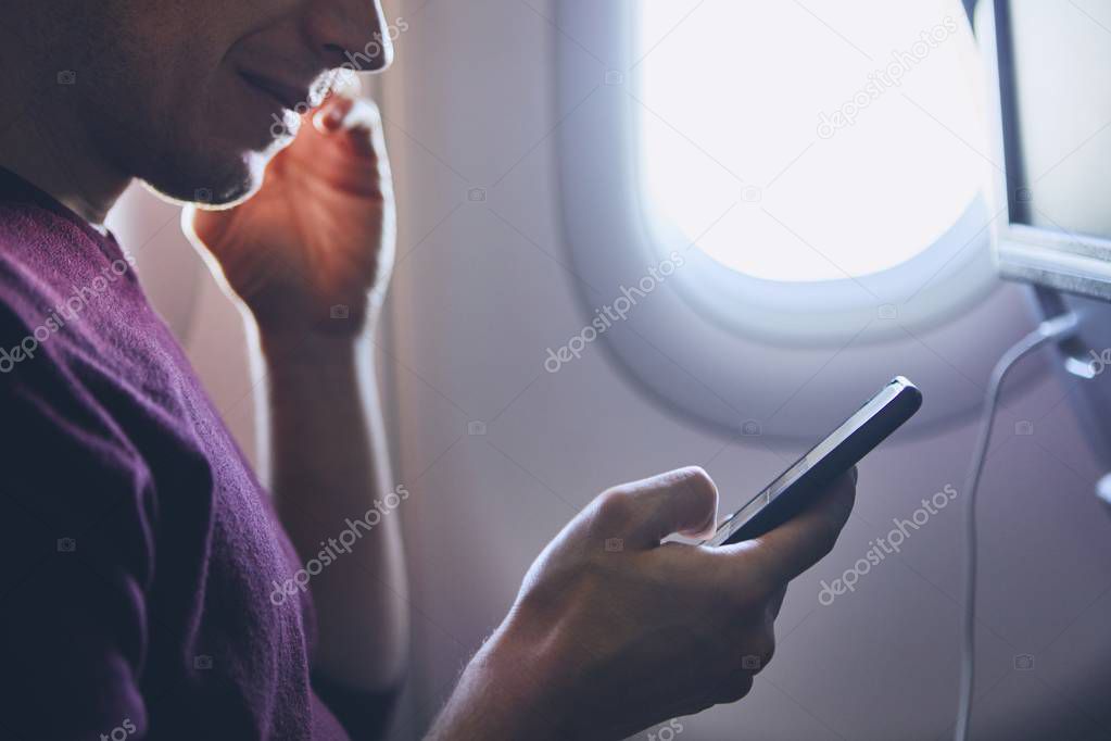 Connection during flight. Young man using mobile phone in airplane.