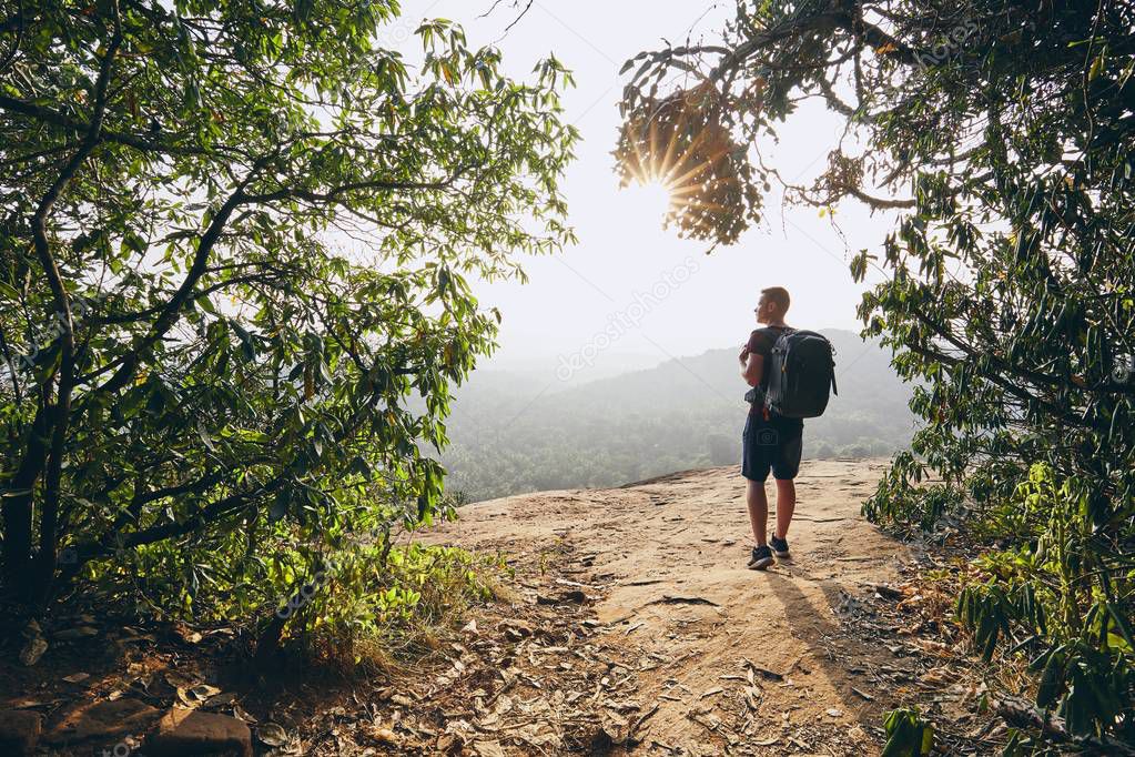 Young hiker overlooking view from rock. Landscape of Sri Lanka at sunset.