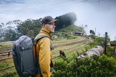 Bulutlarda tren istasyonuna karşı sırt çantalı genç bir adamın portresi. Idalgashinna, Sri Lanka.