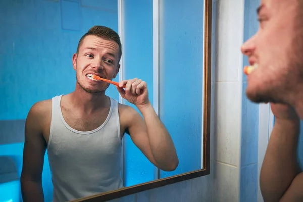 Morning hygiene routine. Man brushing teeth and looking in mirror of home bathroom.