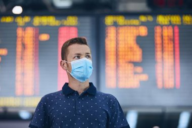 Havaalanının kalkış panosuna karşı yüz maskesi takan adam. Yeni normal, koronavirüs ve kişisel koruma temaları. 