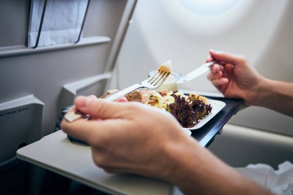 Man eating airline meal served on seat tables during flight.