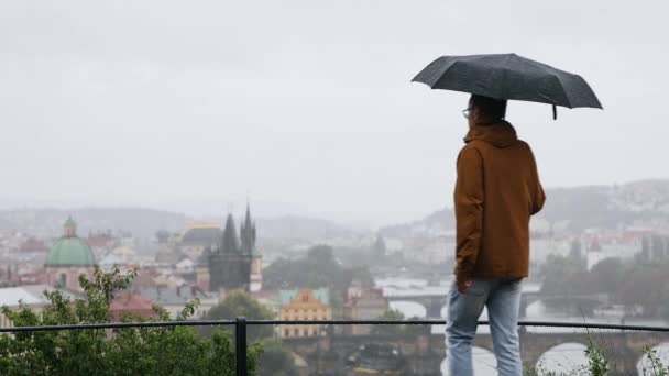 Şemsiyeli genç adam şiddetli yağmurda şehre bakıyor. Çek Cumhuriyeti Prag 'da Hüzünlü Gün