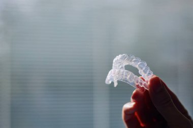 Elin diş beyazlatma tepsilerini pencereye dayadığı yakın çekim görüntüsü.