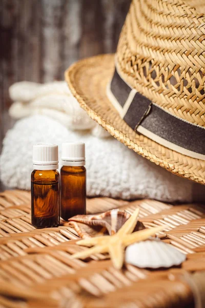 İki masaj yağı şişeleri, beyaz banyo havlusu ve ahşap yüzeyde hasır şapka 