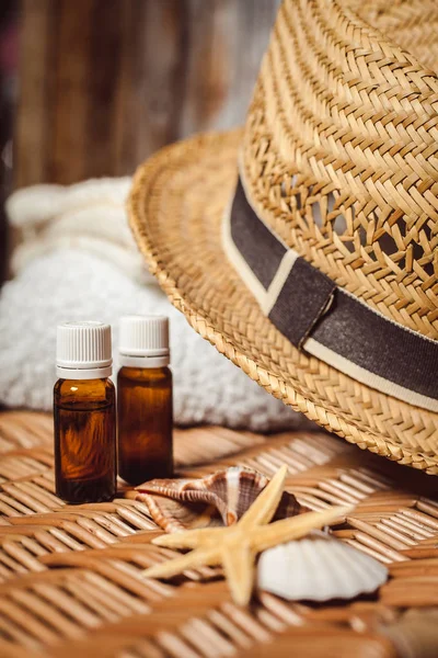 İki masaj yağı şişeleri, beyaz banyo havlusu ve ahşap yüzeyde hasır şapka 