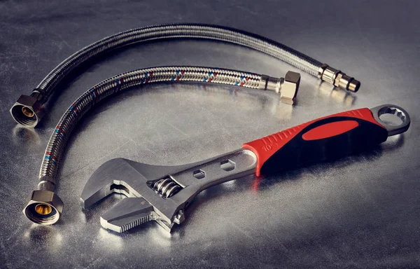 Adjustable wrench and flexible connecting hoses on silver surface, shallow depth of field