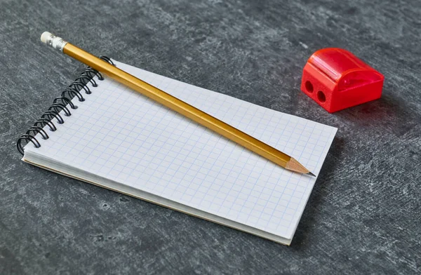 Pencil lies on the notebook next to the sharpener, gray background, shallow depth of field