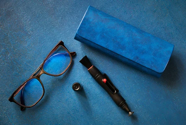 Glasses, glasses case and cleaning handle for optics,  on blue background, top view, shallow depth of sharpness