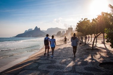 RIO DE JANEIRO, BRAZIL - MAY 24, 2018: People walking on famous sidewalk of Ipanema beach at sunset clipart