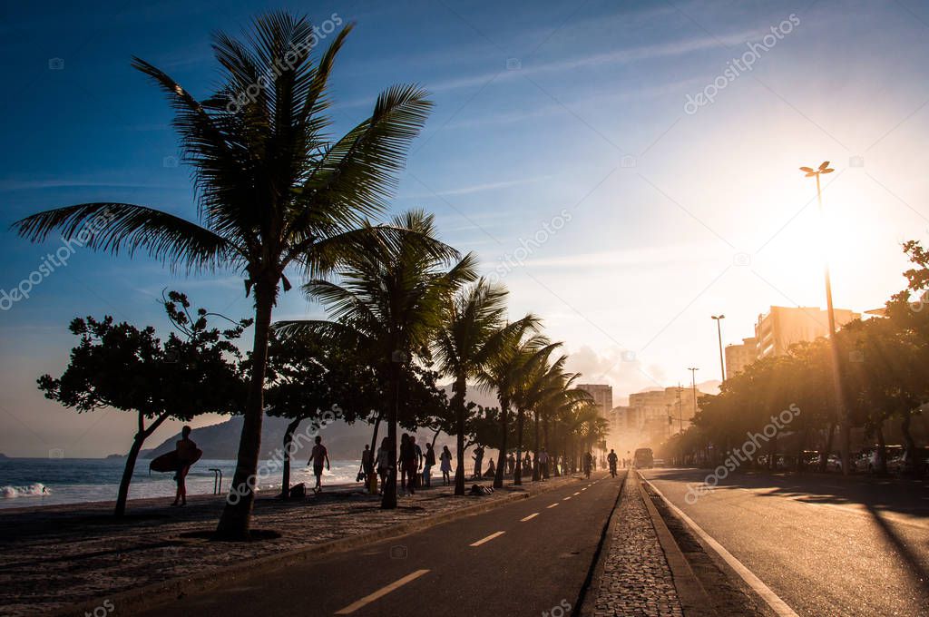 people walking near cycling track and palm trees in Ipanema Beach at Sunset, Rio de Janeiro, Brazil