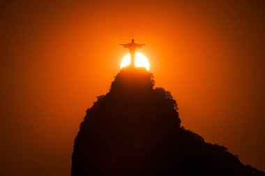 Rio de Janeiro, Brazil - February 1, 2019: Sun setting behind Corcovado mountain with Christ the Redeemer statue on top of it. clipart