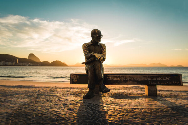 Rio de Janeiro, Brazil - July 1, 2019: Statue of Brazilian poet Carlos Drummond de Andrade sitting on a bench in Copacabana beach by sunrise
