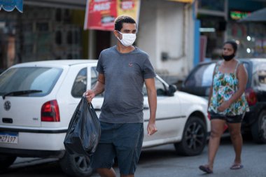 Rio de Janeiro, Brezilya - 3 Temmuz 2020: Kentin banliyölerindeki Coronavirus salgını sırasında insanlar maske takıyor. Siyah plastik çanta taşıyan adam..