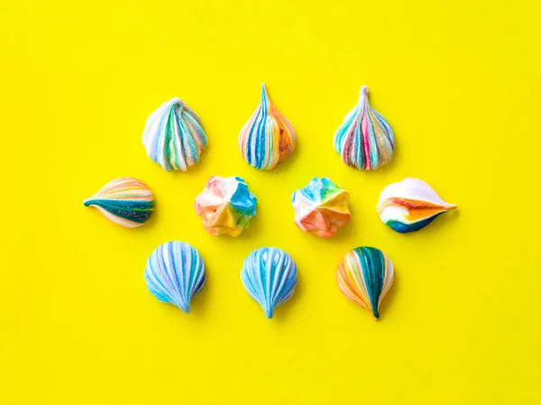 Small multicolored meringue cakes on a yellow background. The style of minimalism. Appetizing meringues. Location of objects in the center. View from above.